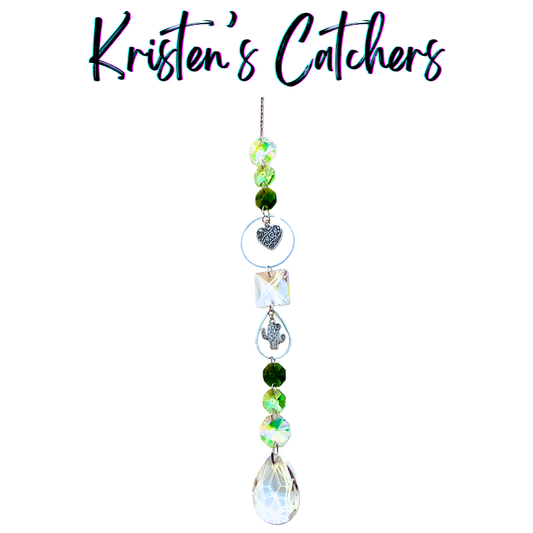 Handcrafted Mother's Day sun catcher with silver cactus charm, filigree heart charm, green gradient beads, clear square crystal, and a lattice-cut teardrop pendant drop.