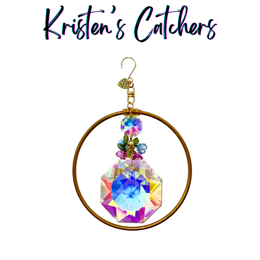 Handcrafted 4-inch ornamental sun catcher with large A/B iridescent octagon crystal, bronze ring frame, and enamel flower charm cluster in pink blue and green.