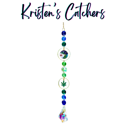Handcrafted single strand sun catcher with illustrated camping night scene pendant, green botanical leaf charm, deep blue teal and green faceted beads, gold hardware, and a large iridescent A/B arrowhead pendant drop