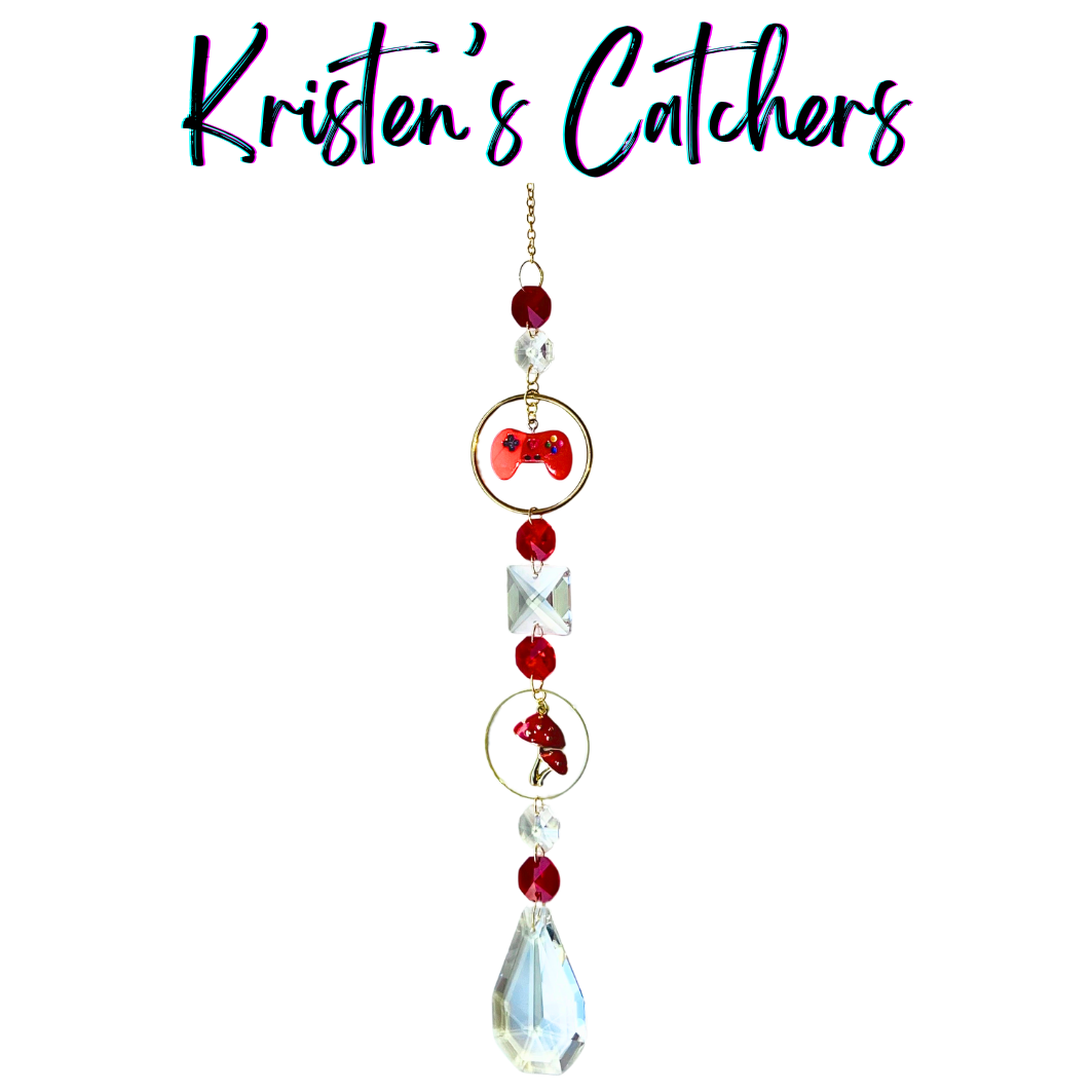 Handcrafted single strand sun catcher with red enamel game controller charm, red mushroom charm, deep red faceted beads, large clear square crystal, gold hardware, and a clear A/B teardrop pendant drop