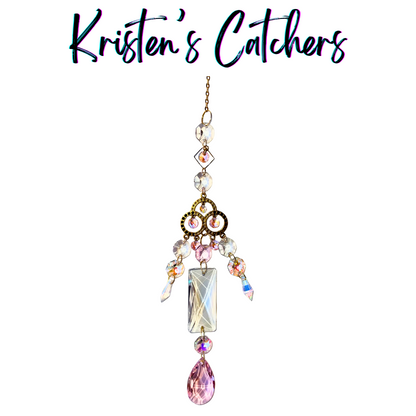 Princess-style sun catcher with ornate gold centerpiece, pink and clear prisms, and pink teardrop finale hanging against white background