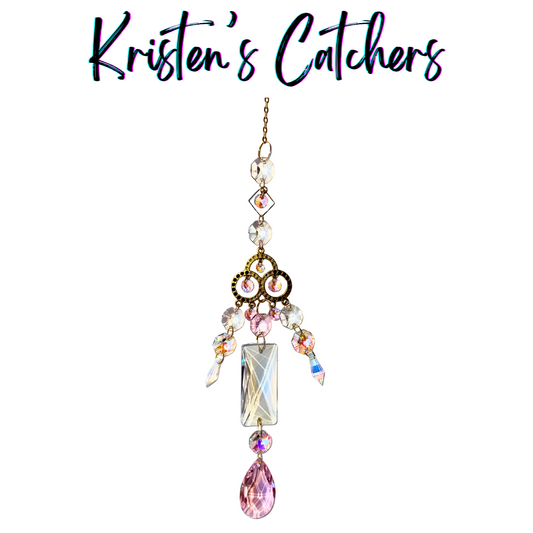 Princess-style sun catcher with ornate gold centerpiece, pink and clear prisms, and pink teardrop finale hanging against white background