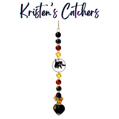 Void Kitty Tribute sun catcher with black cat centerpiece featuring yellow and amber eye-color crystals, black heart crystal, and autumn flowers