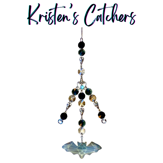 Handcrafted multi-strand sun catcher with four silver bat connector charms, ornate heart connector, black teal and champagne beads, clear crystal accents, and a large iridescent gray geometric bat-shaped prism pendant drop